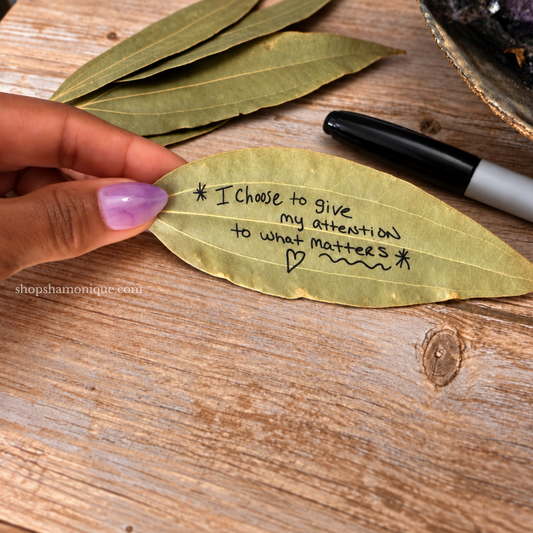 Hand holding an intention bay leaf with “I choose to give my attention to what matters” handwritten on it.